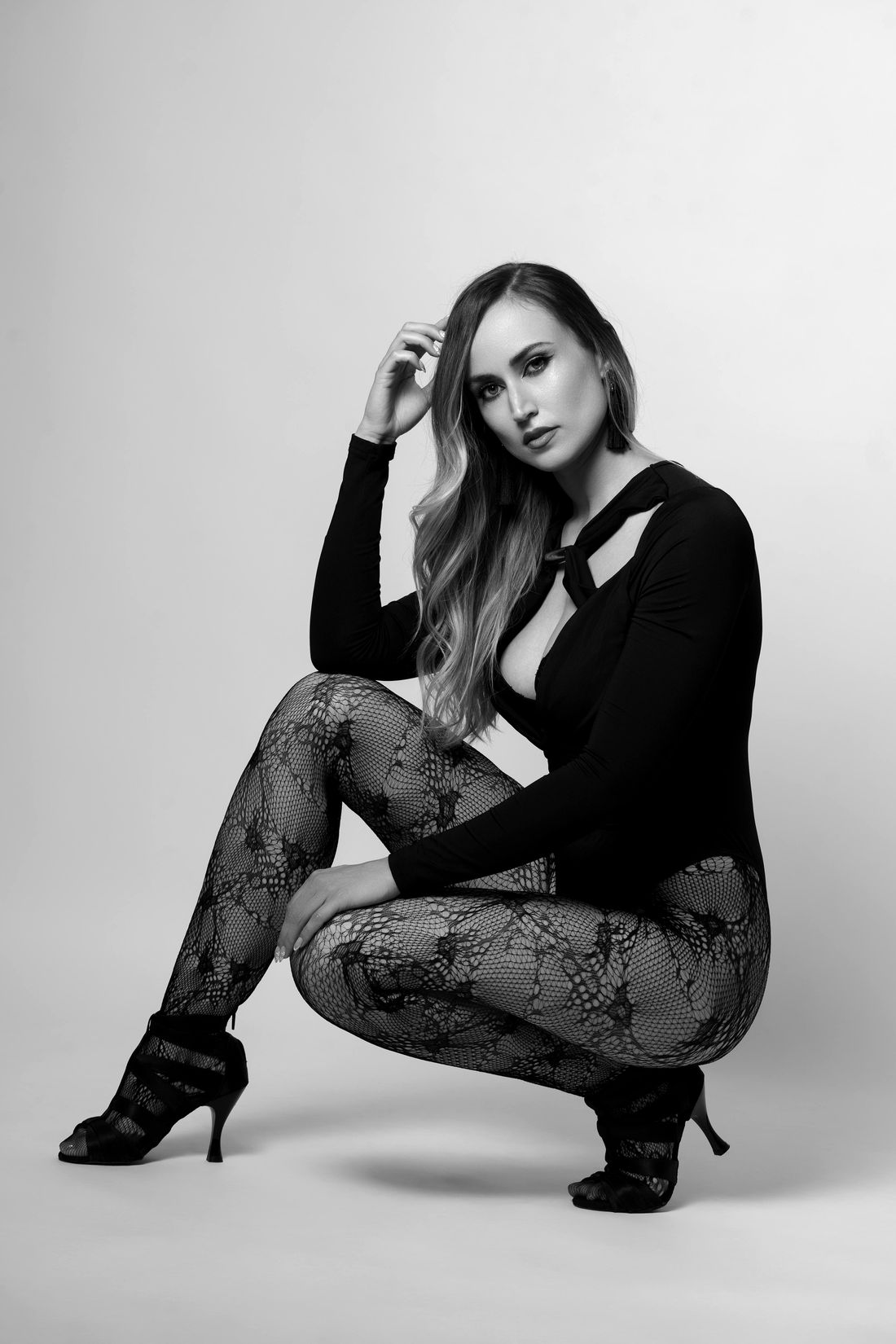 Estefanía Martínez agachada sobre unos tacones, con medias de encaje y una mano en el cabello, mirando a cámara